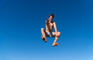 Naklejka premium A young man in a swimsuit leaps into the air like Spider-Man against an intense blue sky, offering plenty of copy space.