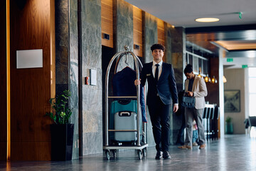 Hotel attendant pushing luggage cart in a lobby and looking at camera.