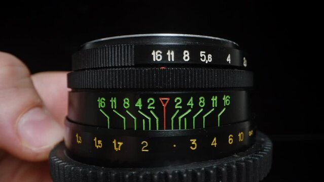 An old photo lens, a man adjusts the focus and it protrudes outward. Green numerical markings. Close-up.