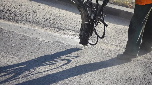 Road worker using specialized equipment embeds small pits on the asphalting of road surfaces.