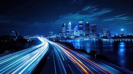 Obraz premium City at night, with its iconic skyline illuminated against a deep blue sky, featuring a bustling highway overpass adorned with motion-blurred cars traversing the scene.