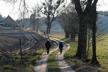 Two walking people on winding rural road in spring scenery