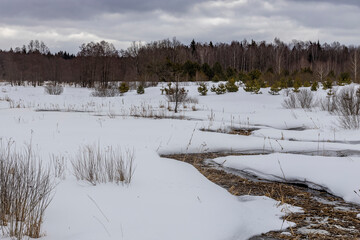 A winding small river in the middle of a snowy field, a winter landscape on a cloudy day, the concept of changing nature, a winding stream, a winding line composition in space