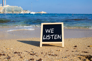 We listen symbol. Concept words We listen on black chalk background. Beautiful sea background....