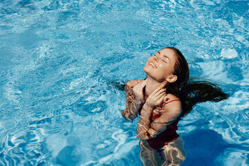 Happy woman swimming in the pool in red swimsuit with loose long hair in the sunshine, skin...