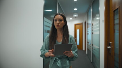 Woman ceo searching tablet computer in office. Manager walking through corridor