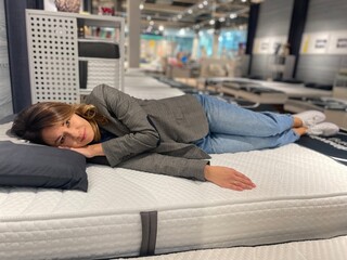 Close up of Caucasian beautiful female customer lying on bed in furniture store choosing new bed for home. Pretty young female resting on bed in shopping center. Shop concept - Powered by Adobe