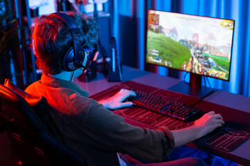 Host channel of young gaming streamer, team gamer playing battle game shooting with multiplayer at warship on pc screen with back side image, wearing headset with mic at digital neon room. Gusher. - obrazy, fototapety, plakaty