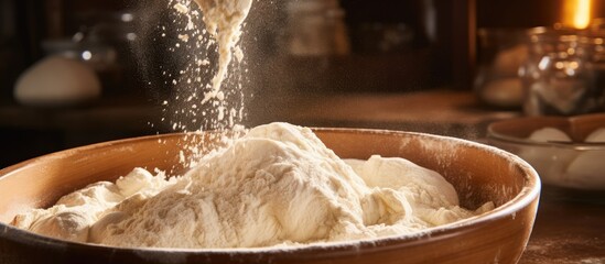 An image of flour being poured from a container into a bowl that is already on a table, displaying a cooking process - obrazy, fototapety, plakaty