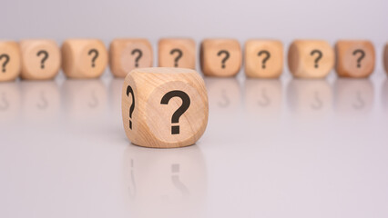 in the foreground is one wooden cube with a question mark and a reflection from the table surface. in the background is a row of wooden cubes with a question mark out of focus.