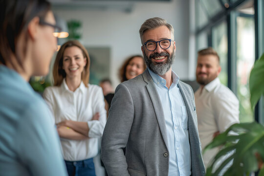 Successful Corporate Team: A Business man in a gray jacket and blue shirt smiles at the camera, Diverse Professionals Unite with Confidence and Leadership in Modern Office Setting