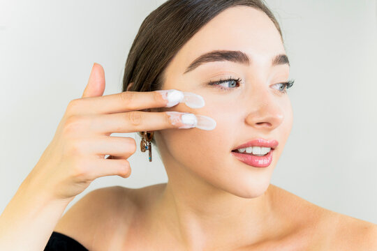 Beautiful woman applying moisturizer cream on her face. Closeup happy young woman applying cream to her face Skincare and cosmetics concept.