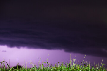 Lightning flashes across the night sky on the field grass. Violet color. Weather changes concept
