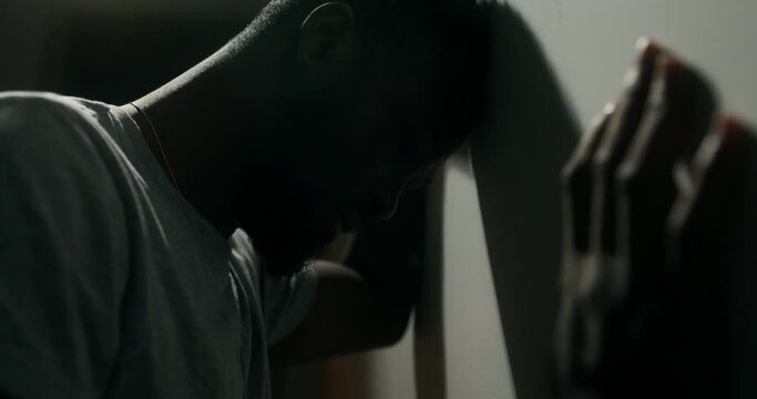 A bearded man in casual clothes screams and punches against the wall out of anger standing indoors