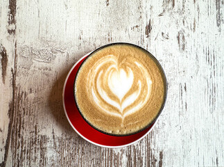 Closeup red cup of  coffee with heart art decoration on a bright wooden table