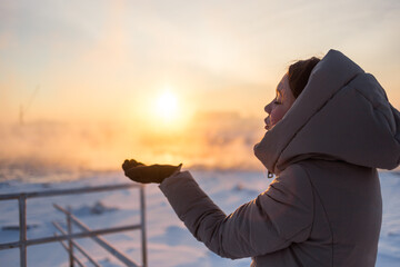 A woman blowing the sun in her hand, happy in snowy landscape