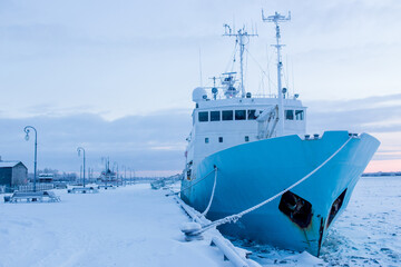 A big boat with blue and white colors is anchored in the snowy landscape