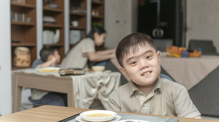 a smiling seven-year-old boy with Down syndrome sits at a table with books in a home interior - 764295261
