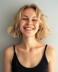 portrait of a laughing blonde girl in a black dress with straps on a gray background - 764295846