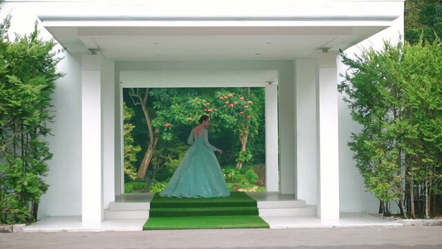 Elegant woman in a green dress standing in a white gazebo surrounded by lush greenery.