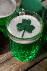 St. Patrick's day party. Green beer with decorative clover leaf and leprechaun hat on wooden table,...
