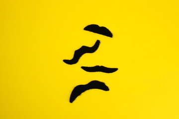 Different fake mustaches on yellow background, flat lay