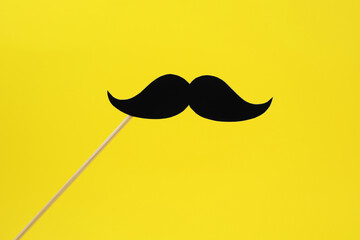Fake paper mustache on stick against yellow background