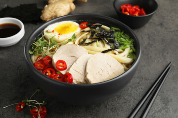 Delicious ramen with meat in bowl and ingredients on grey textured table, closeup. Noodle soup