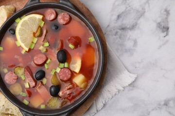 Meat solyanka soup with thin dry smoked sausages in bowl on white marble table, top view. Space for text