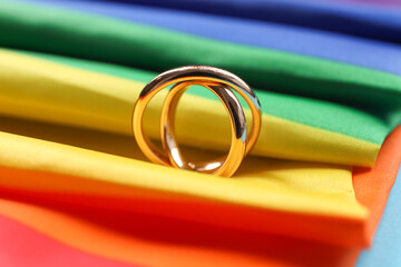 Rainbow LGBT flag and wedding rings on light blue background, closeup