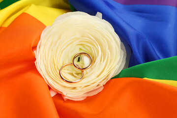 Wedding rings and flower on rainbow LGBT flag, closeup