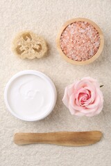 Flat lay composition with moisturizing cream in open jar and other body care products on light textured table