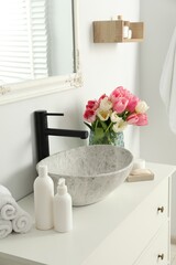 Obraz na płótnie Canvas Vase with beautiful pink tulips and toiletries near sink in bathroom