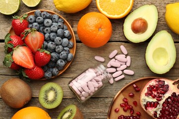 Vitamin pills in bottle and fresh fruits on wooden table, flat lay