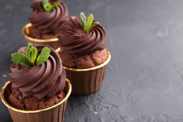 Delicious chocolate cupcakes with mint on black textured table, closeup. Space for text