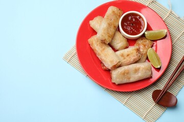 Tasty fried spring rolls, lime and sauce served on light blue table, top view. Space for text