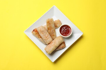Fried spring rolls and sauce on yellow table, top view