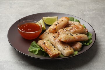 Tasty fried spring rolls with lettuce, lime and sauce on gray table