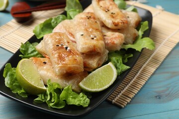 Tasty fried spring rolls, lettuce and lime on light blue wooden table, closeup