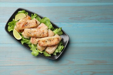 Tasty fried spring rolls, lettuce and lime on light blue wooden table, top view. Space for text