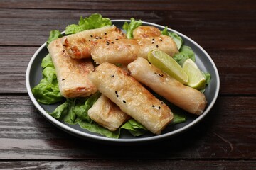 Tasty fried spring rolls, lettuce and lime on wooden table