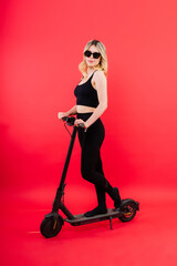 Fototapeta na wymiar Blonde woman on red white background sitting on electro scooter and resting, copy space