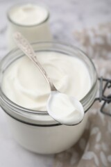 Fototapeta na wymiar Delicious natural yogurt in glass jar and spoon on table, closeup