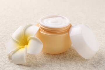 Body care. Moisturizing cream in open jar and flower on light textured table, closeup