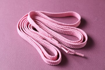 Stylish pink shoe laces on violet background, closeup