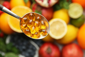 Vitamin pills in spoon over fresh fruits, top view. Space for text