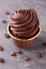 Delicious chocolate cupcake and coffee beans on grey textured table, closeup