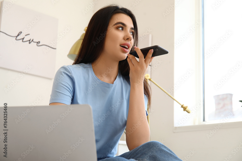 Poster female freelancer with mobile phone recording voice message in bedroom