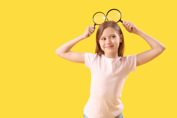 Funny little girl with magnifiers on yellow background