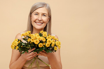Attractive, senior 60 year old woman wearing lingerie holding beautiful bouquet of chrysanthemums